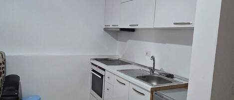 A compact kitchen with white cabinets, a stove, a sink, and a dishwasher.