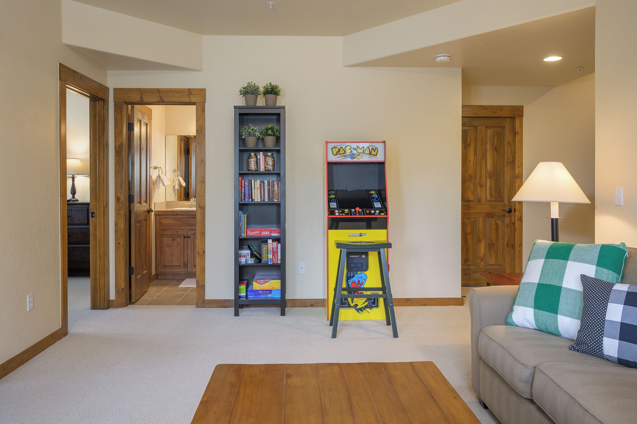 A living room with a sofa, a lamp, a bookshelf, and a Pac-Man arcade machine.