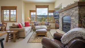 Un salon chaleureux avec une cheminée en pierre, une grande fenêtre donnant sur les montagnes et un coin salon confortable.