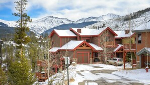Un chalet niché dans un paysage enneigé, avec des cabanes en bois et une chaîne de montagnes en toile de fond.