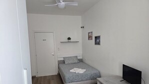 Une chambre à coucher comprenant un lit, un bureau, une télévision, un ventilateur de plafond et une porte.