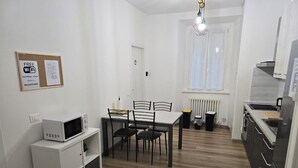 Une cuisine compacte équipée d’un four à micro-ondes, d’une table et de chaises. On y trouve également un tableau d’affichage avec un symbole Wi-Fi, un radiateur et une fenêtre avec des rideaux.