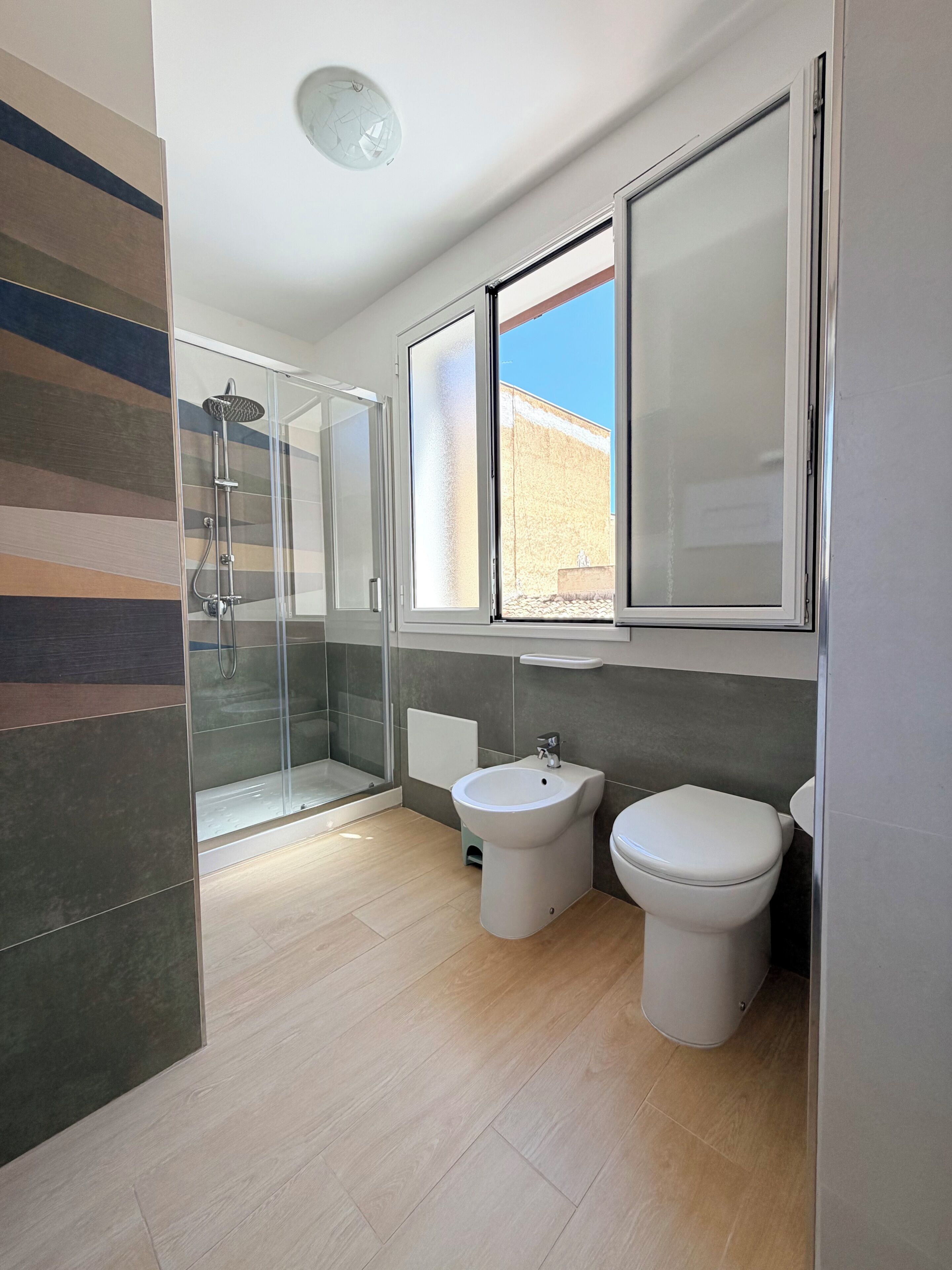 A modern bathroom with a shower, bidet, toilet, and a window with a view.