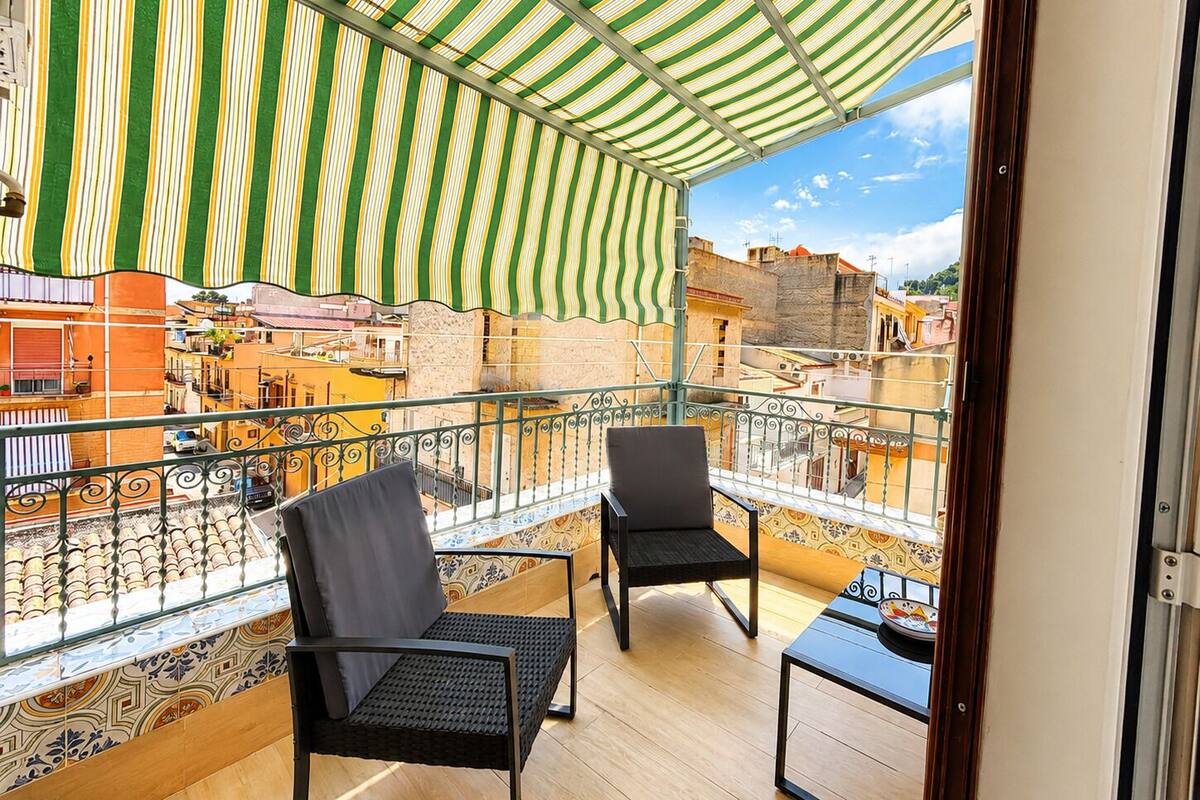 A balcony with two chairs, a small table, and a striped awning.