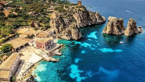 A coastal town with clear blue waters, rocky outcrops, and a historic tower. - B&B Le Venere Rooms (Castellammare del Golfo)