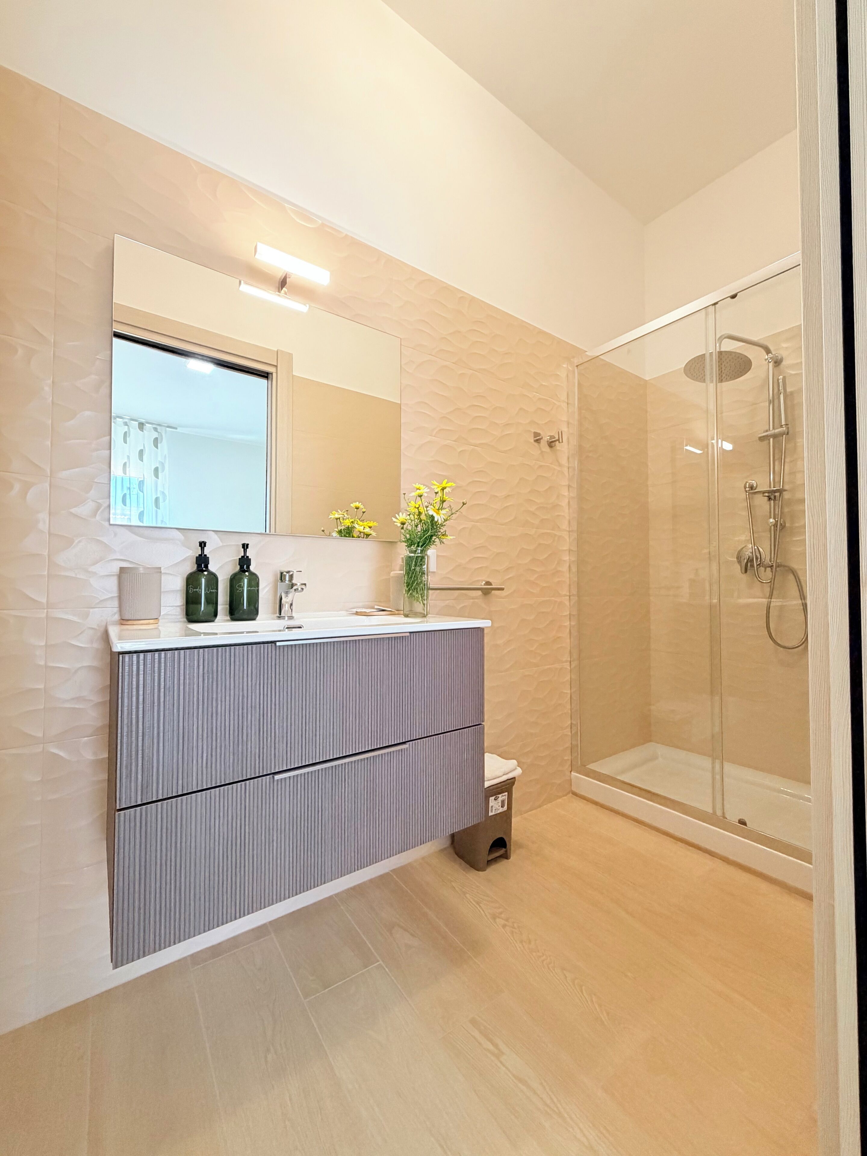 Un baño moderno con tocador, espejo, ducha y un pequeño cubo de basura.