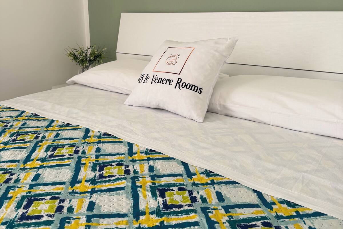 A bed with a patterned bedspread, two pillows, and a wall-mounted light fixture.
