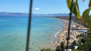 Una playa con agua azul cristalina, una orilla arenosa y vehículos recreativos estacionados al frente.