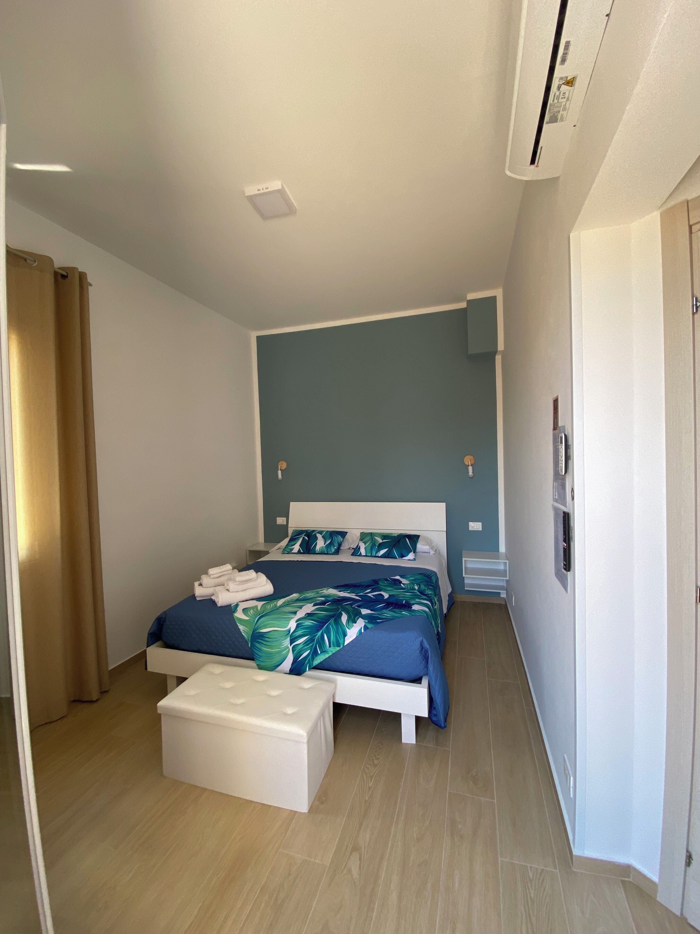 Una habitación de hotel moderna con una cama grande, una mesita de noche, una mesita auxiliar y un ventilador de techo, además de una puerta.