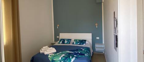 Una habitación de hotel moderna con una cama grande, una mesita de noche, una mesita auxiliar y un ventilador de techo, además de una puerta.