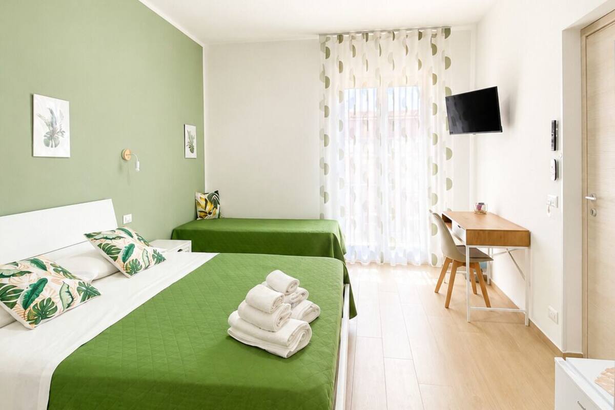 A hotel room with two beds, a desk, a television, and a window with curtains.