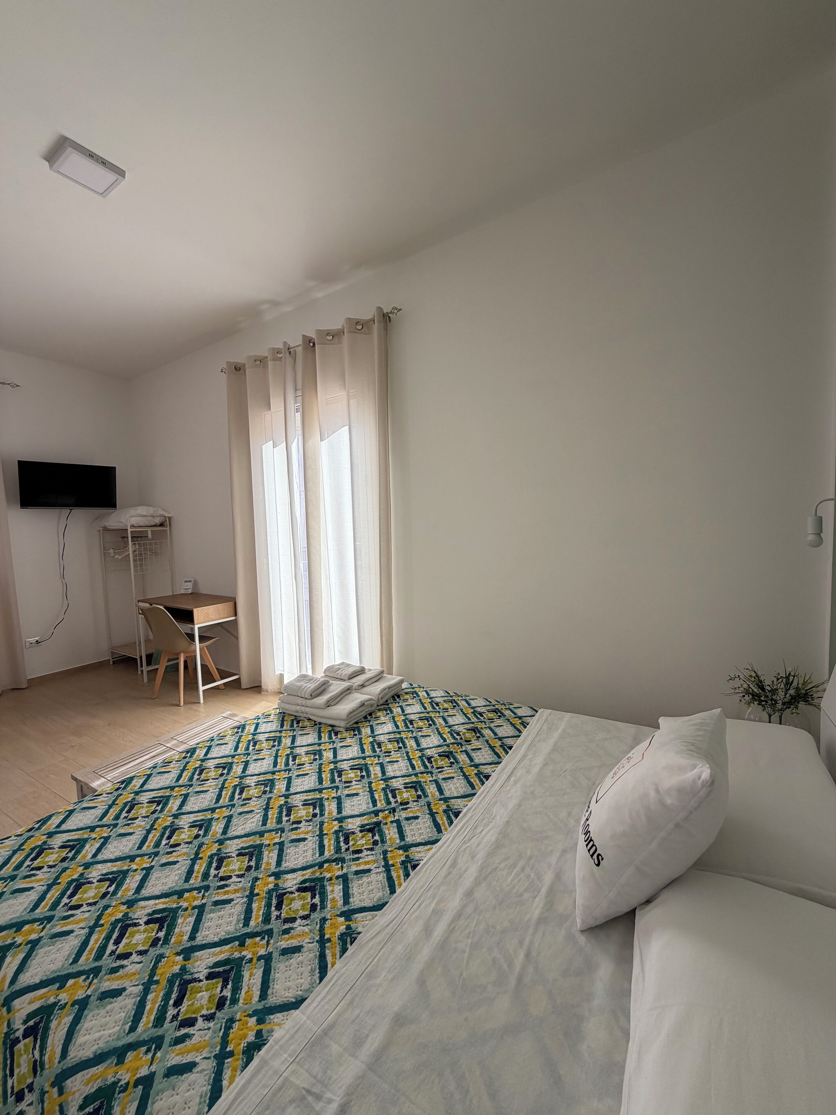 Une chambre d’hôtel avec un lit, un bureau, une chaise, une télévision et une fenêtre avec des rideaux.