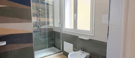 Un baño moderno con cabina de ducha de vidrio, un lavabo blanco y un inodoro.