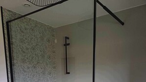 Eine begehbare Dusche mit Glaswänden, gefliestem Boden und einer Wand mit Blumenmuster.