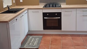 Eine moderne Küche mit Einbauherd, Backofen und Geschirrspüler, mit einer gefliesten Spritzwand und einer Leuchte über der Arbeitsfläche.