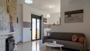 A modern living room with a fireplace, a sofa, a coffee table, and a dining area in the background. - Three Waves Maisonettes Elena (Agios Nikolaos)