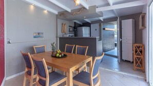 A dining area with a wooden table and chairs, a fruit bowl, and a kitchen in the background. - Three Waves Maisonettes Elena (Agios Nikolaos)