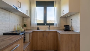 Een compacte keuken met houten kastjes, een gasfornuis, een gootsteen en een raam met gordijnen.