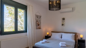 Een slaapkamer met een bed, twee nachtkastjes met lampen, een raam met gordijnen, een wandairconditioner en een decoratief object boven het bed.