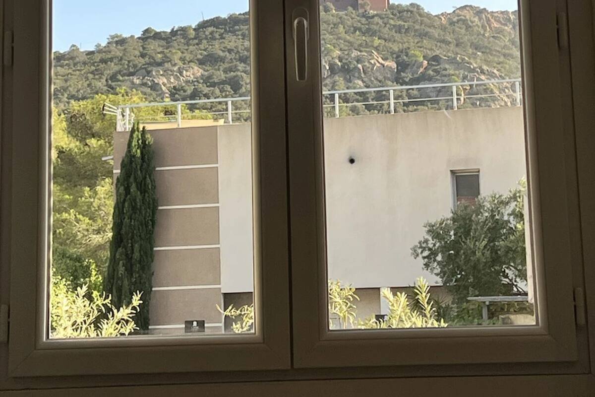 A view through a window with a clear sky, a building with a tower, and a hillside with vegetation.