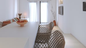 Un espace repas moderne avec une longue table, des chaises en osier, des luminaires suspendus et une vue sur l’extérieur grâce à de grandes fenêtres.