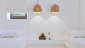 A modern, minimalist bedroom with two white beds, a built-in bench, and two hanging wicker lamps. - 2-bedroom Villa Kalypso (Antiparos)