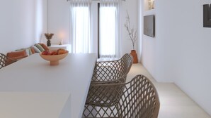 A modern dining area with a long table, wicker chairs, pendant lights, and a view through large windows. - 2-bedroom Villa Kalypso (Antiparos)