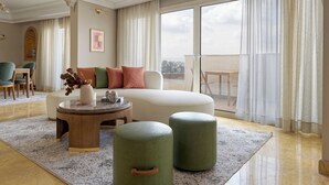Un salon spacieux doté d’une grande fenêtre, d’un canapé, de plusieurs poufs et d’une table basse.