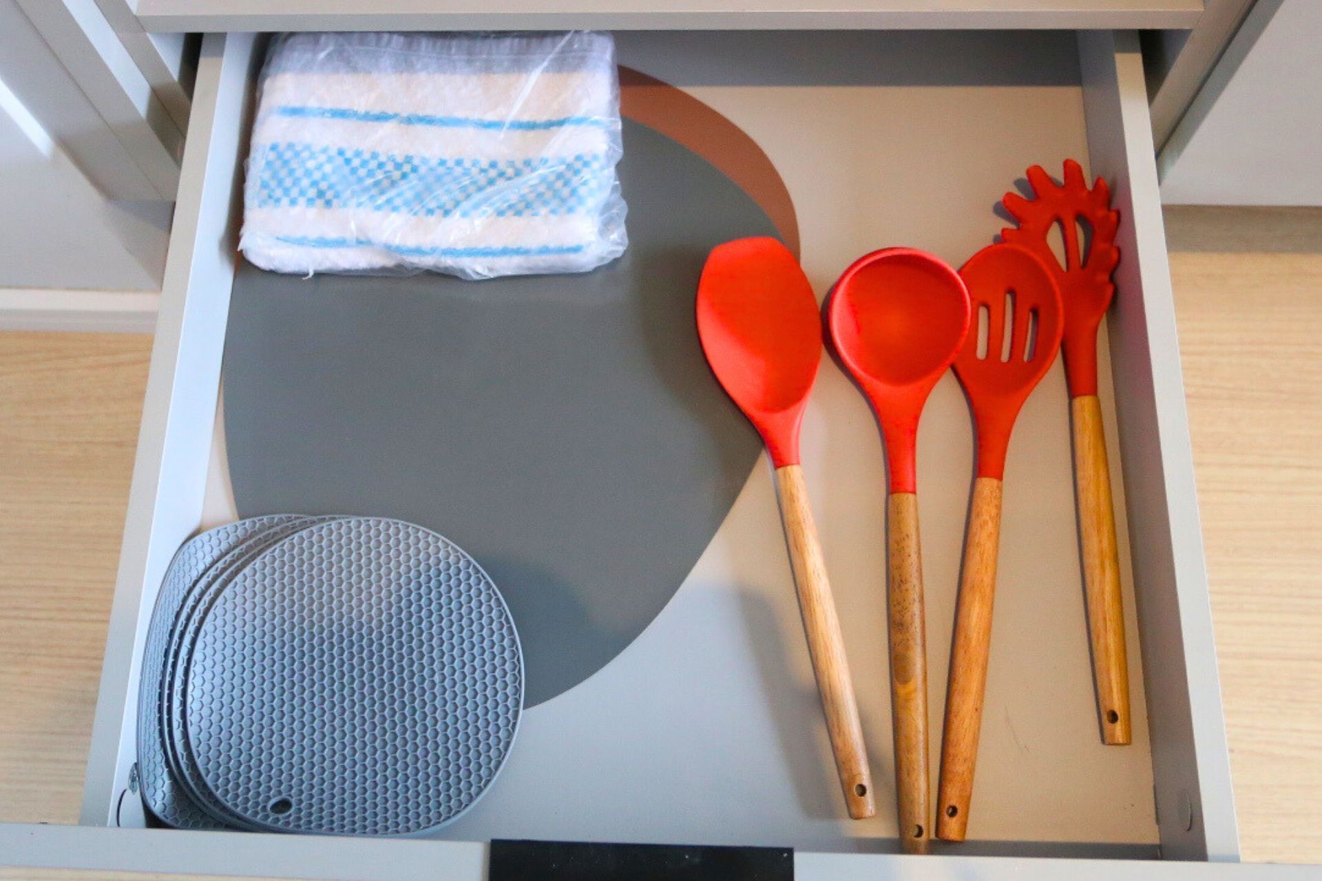 A kitchen drawer with a blue and white checkered towel, a non-stick griddle, and red kitchen utensils.