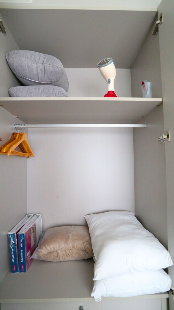 A compact room with a bed, two pillows, a mannequin head, a shelf with a red object, and a set of books.