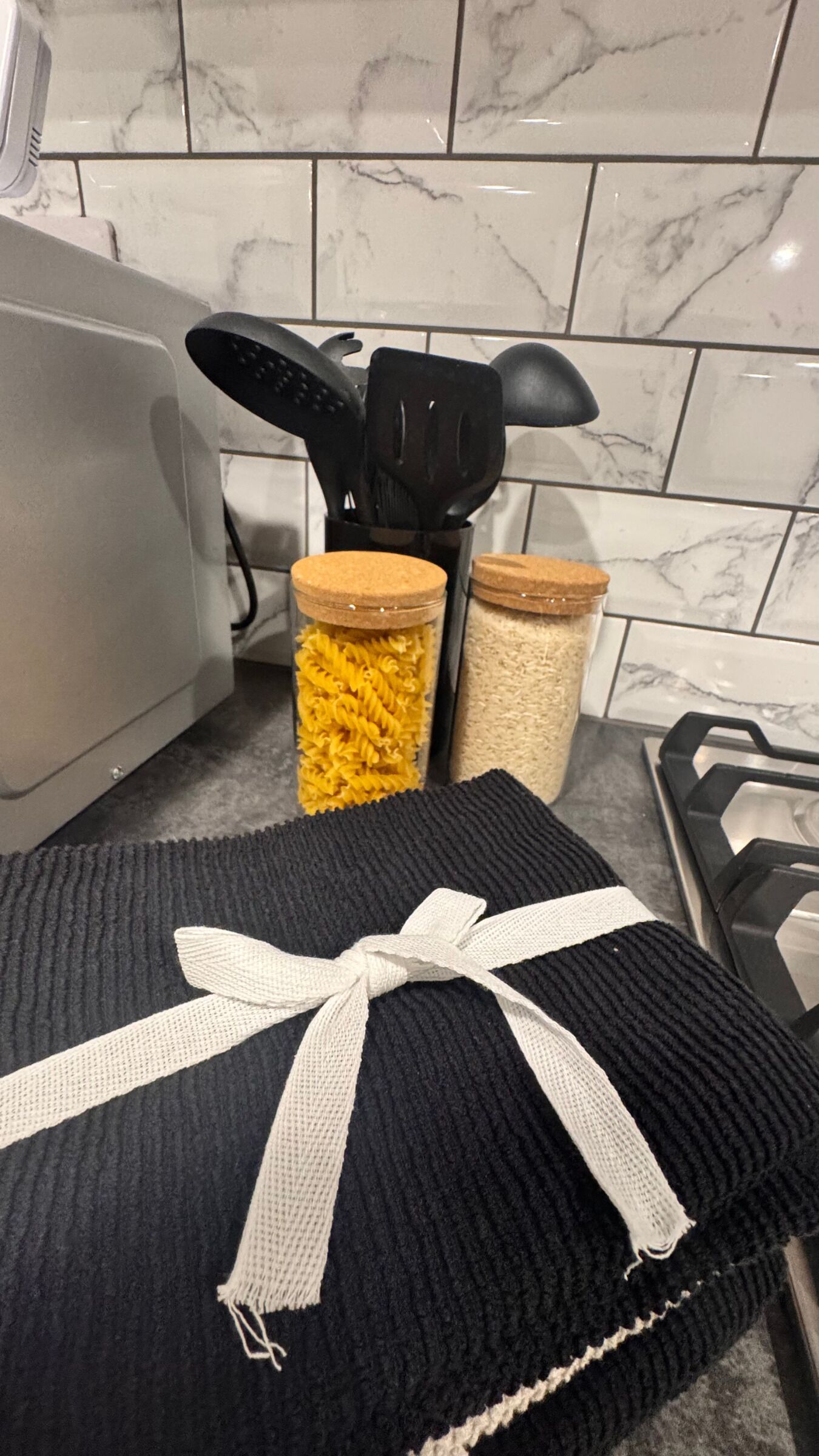Een keuken met een zwarte mat, twee potten pasta en een zwarte spatelhouder.