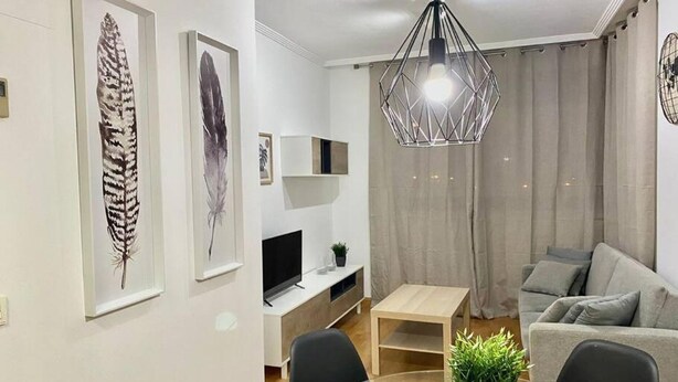 Una sala de estar moderna con un televisor de pantalla plana, una mesa de centro, un sofá e iluminación colgante.