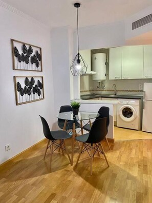 A modern kitchen with white cabinets, a built-in washing machine, and a dining area with a glass table and black chairs.