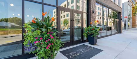A modern building with large glass windows, a brick facade, and two potted plants with flowers.