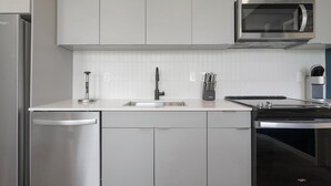 A modern kitchen with white cabinetry, a stainless steel sink, a dishwasher, a microwave, and a stove.