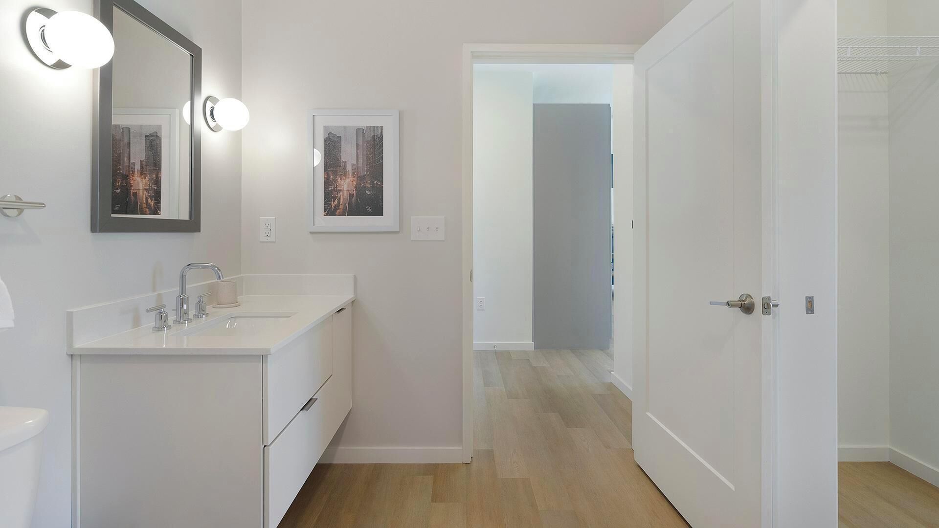 A modern bathroom with a white vanity, a large mirror, and two framed pictures on the wall.