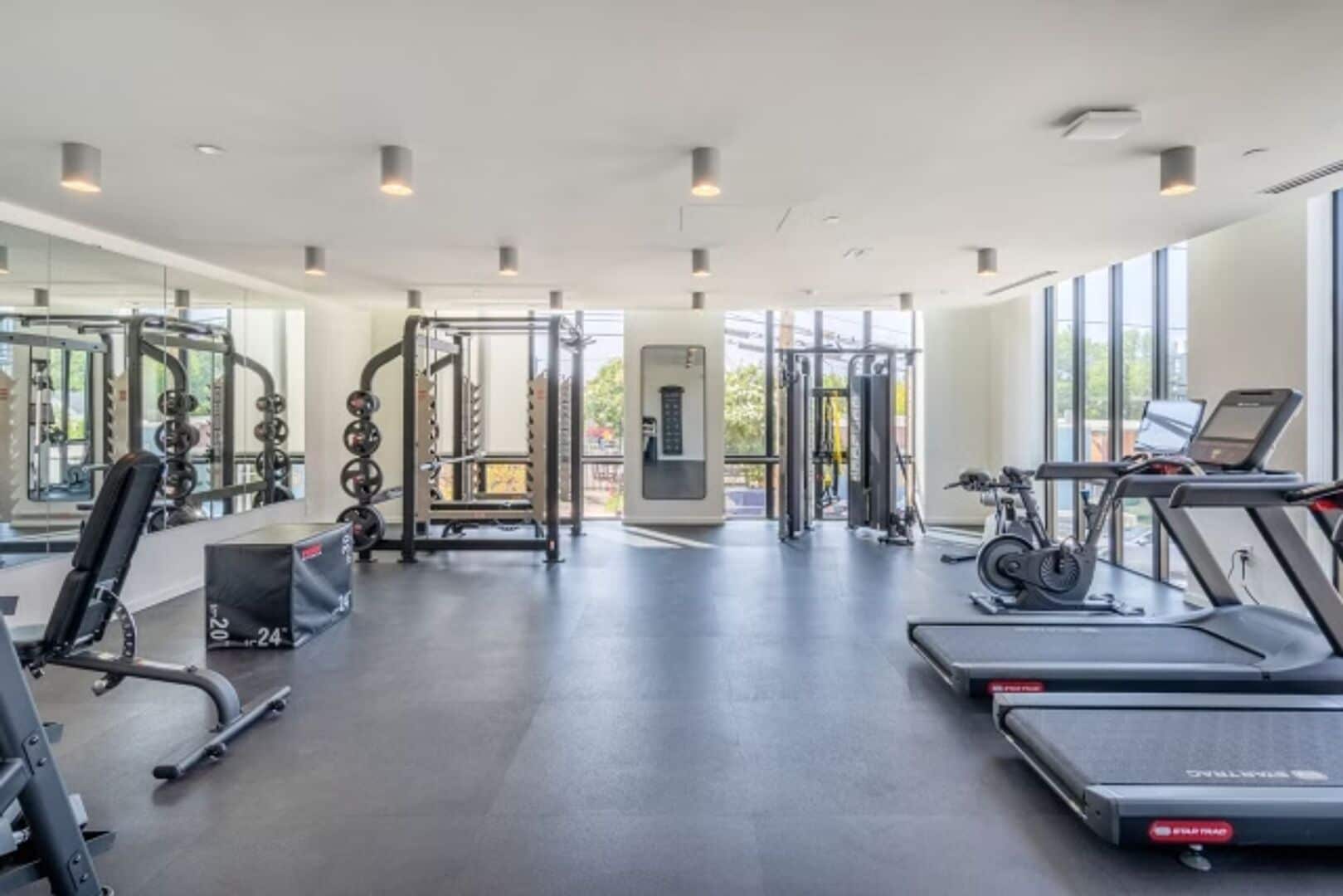 A modern gym with various exercise equipment, large windows, and a clean, spacious layout.