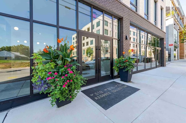 A modern building with large glass windows, a brick facade, and two potted plants with flowers.
