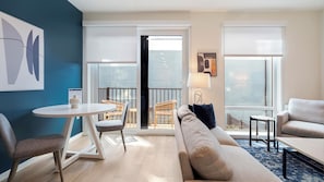 A modern living room with a sofa, chairs, a small table, and a balcony with wicker furniture.
