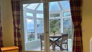 Ein Wintergarten mit Tisch, Stühlen, einem kleinen Holzschrank und Blick ins Freie.