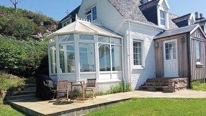 Ein Haus mit Wintergarten, einer Terrasse mit Stühlen und einem gepflegten Rasen.