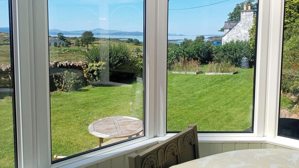 Ein Zimmer mit großen Fenstern, das einen Blick auf einen grünen Garten und eine entfernte Landschaft bietet.
