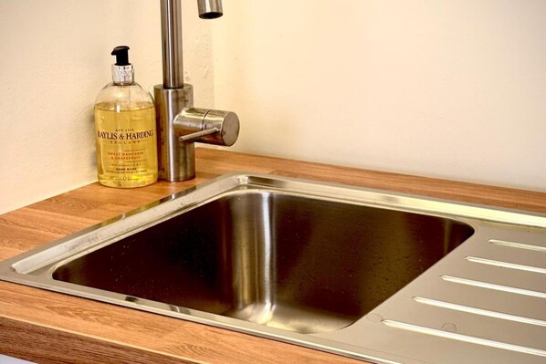 A stainless steel kitchen sink with a modern faucet and a bottle of Baylis & Harding soap on the counter. - 5 Guests - 2 Bedrooms - Free Parking - 1min Beach (Llandudno)