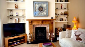 Een woonkamer met een open haard, televisie en planken met diverse decoratieve objecten.