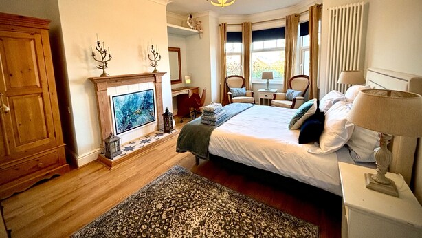 Een slaapkamer met een bed, een open haard, een bureau en een raam met gordijnen.