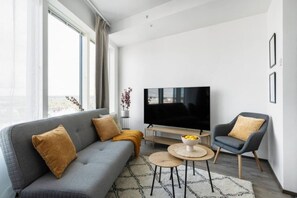 Un salon moderne avec un canapé gris, une petite table basse ronde, un téléviseur et un fauteuil gris.