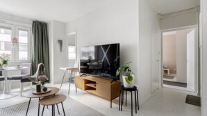 Una sala de estar moderna con un televisor de pantalla plana, un mueble bajo de madera, una zona de comedor con una mesa y sillas, y un ventanal con cortinas.