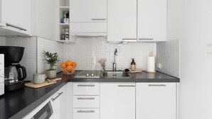 Una cocina moderna con armarios blancos, encimera negra, cafetera, cesta de naranjas y planta en maceta.