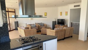 Een moderne keuken met een inbouwfornuis, oven en magnetron, een eethoek met rieten meubels en een flatscreen televisie.