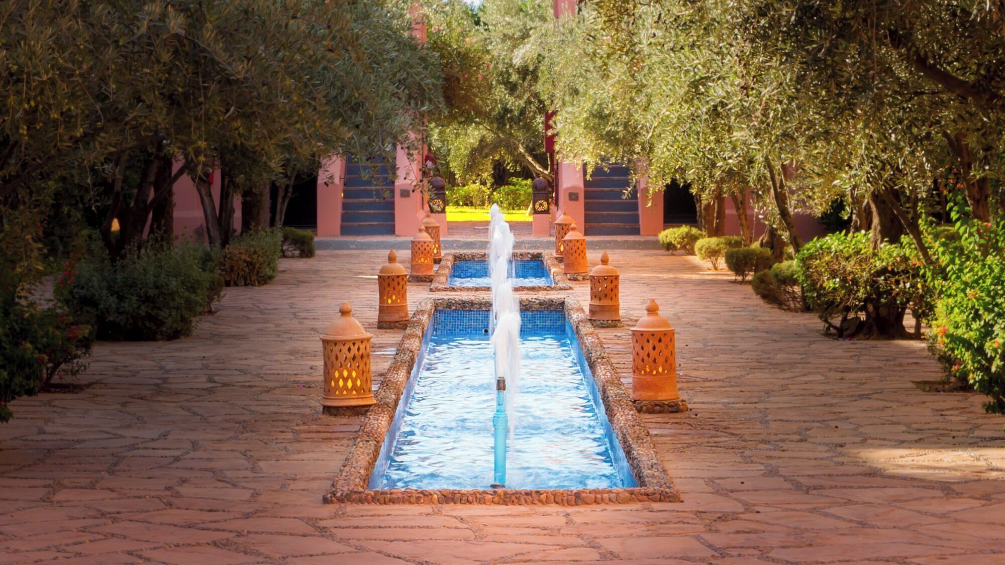 A water feature with a central fountain, surrounded by lanterns and a paved walkway.